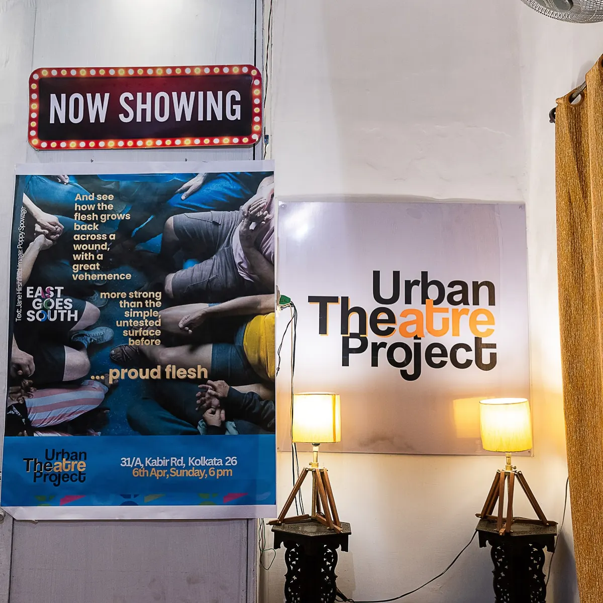 The lobby: a red Now Showing sign above a poster, two brass lamps either side of the Urban Theatre Project board.