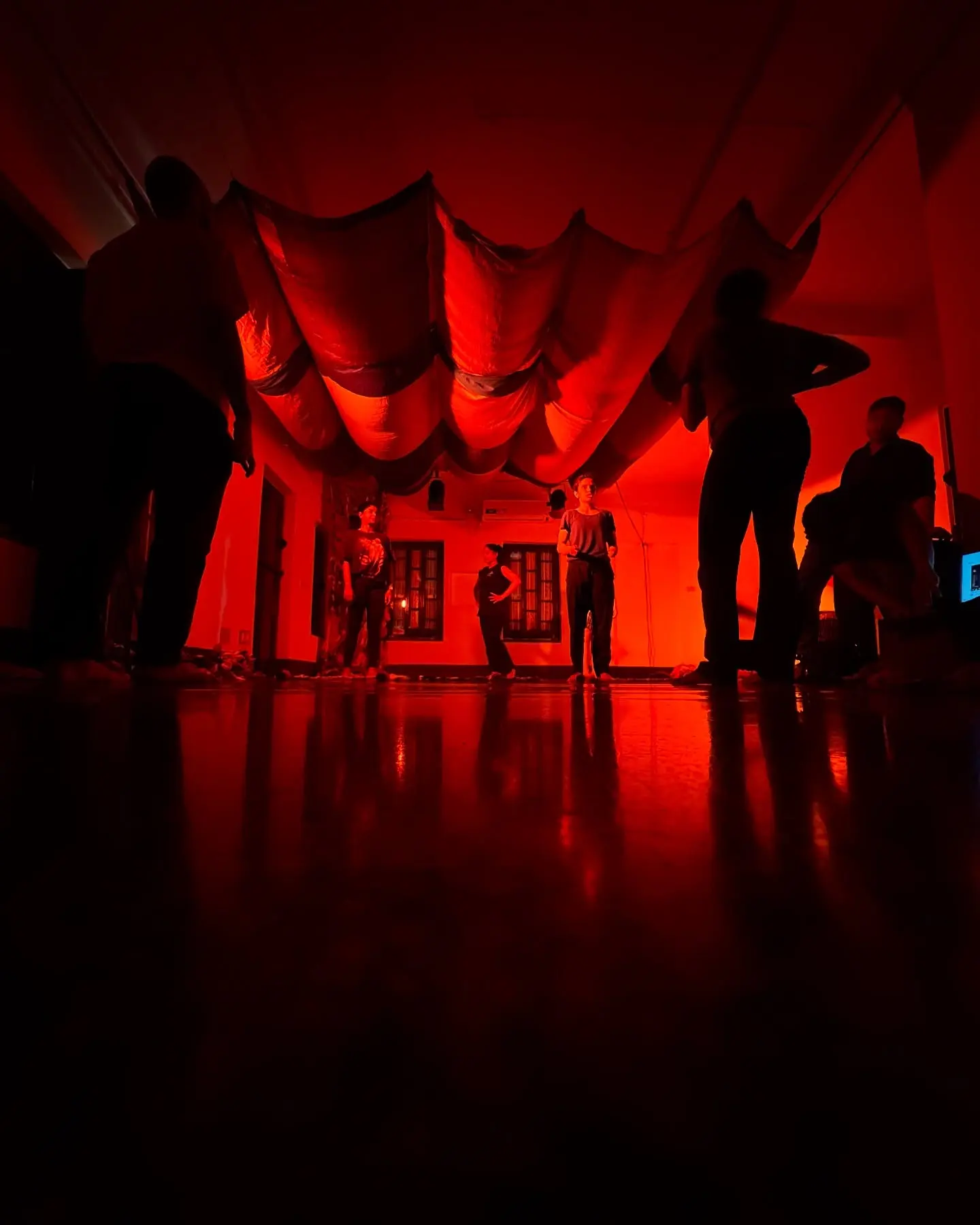 Performers in silhouette under deep red light, the marble floor reflecting them.