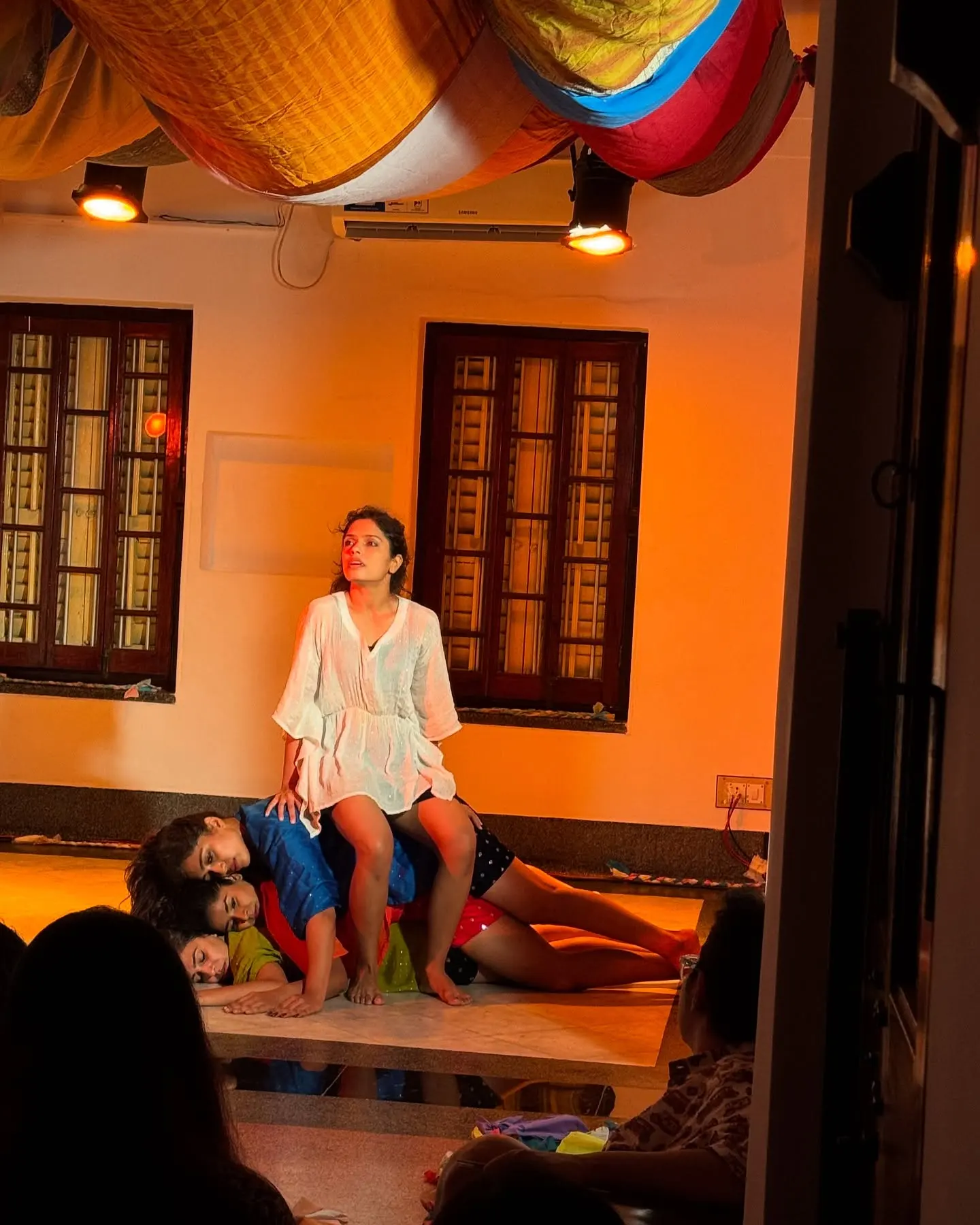 A performer seated on the floor under amber light, the audience a few feet away.