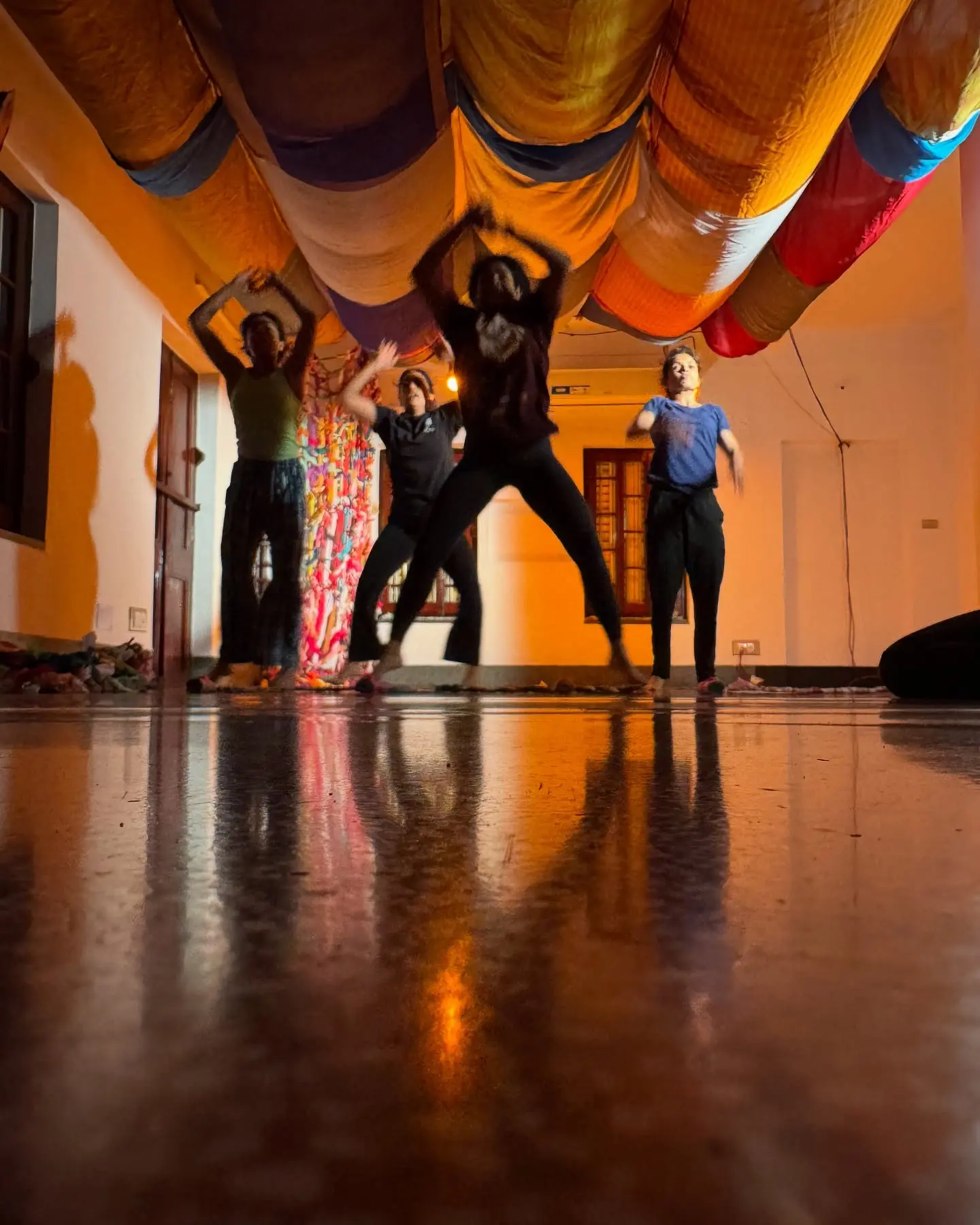 Dancers mid-leap under saris draped from the ceiling, the studio lit amber.